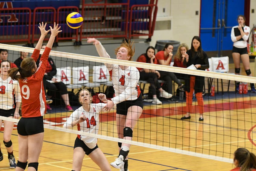 Middle hitter Hannah Helm, #4, leaps into the air to send the ball over the net for Acadia as setter Regan Herrington, #14, looks on.