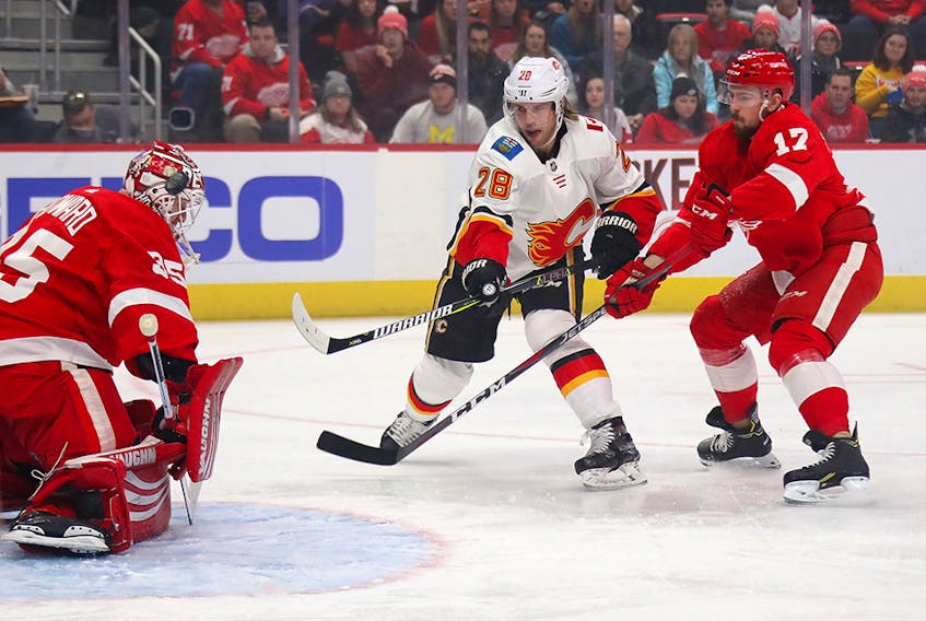 DETROIT, MICHIGAN - JANUARY 02:  Elias Lindholm #28 of the Calgary Flames gets a first period shot off between Filip Hronek #17 and Jimmy Howard #35 of the Detroit Red Wings at Little Caesars Arena on January 02, 2019 in Detroit, Michigan. (Photo by Gregory Shamus/Getty Images)