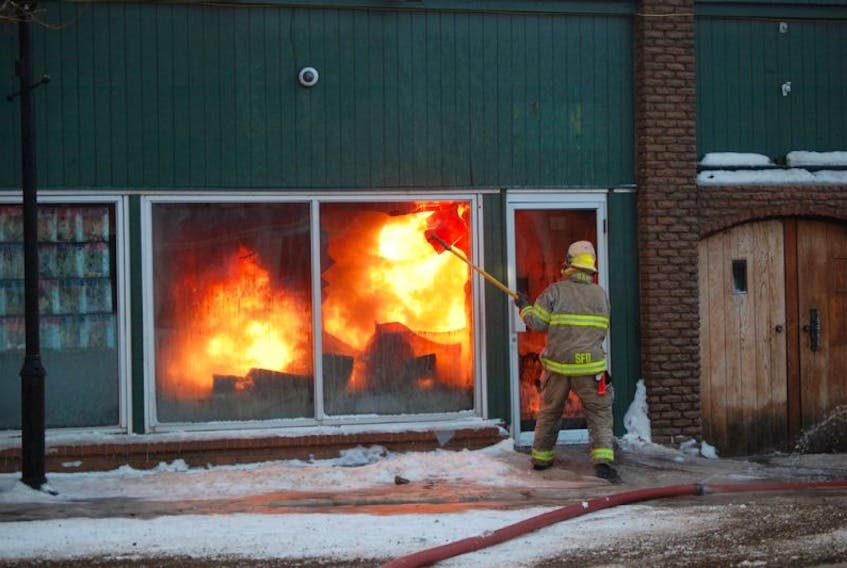 Firefighter Craig Harnum uses a long-handled pick to break out a window in Happy Warriors Yoga to give other firefighters an opportunity to spray water on the fire inside the 104 Main St. building fire in Stephenville on Friday.