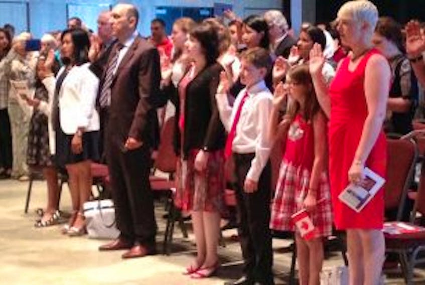 ['New Canadians take the oath of citizenship during a ceremony at Pier 21 on Canada Day.']