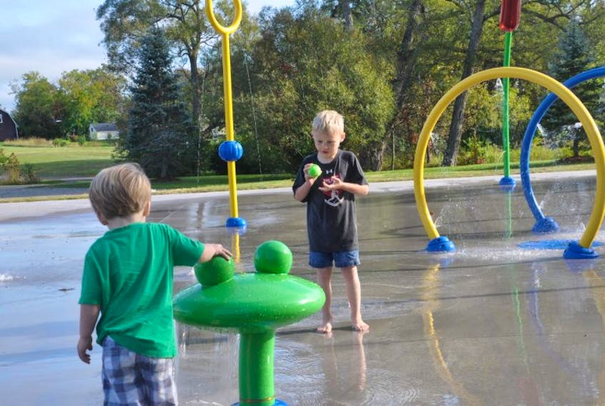 Aiden Curtis, left, inspects one of the spray structures as his older brother Marcus enjoys cooling off at the Acadia Park splash park in Westville. The park will soon be equipped with handicapped parking, thanks to the donation of land from Charles Facey, a local resident.