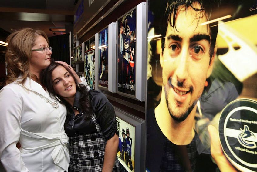 Suzanne Boucher, left, mother of the late Vancouver Canucks' defenceman Luc Bourdon, embraces Charlene Ward (Luc's girlfriend at the time), as they look at his photo on a tribute wall unveiled by the Canucks on Oct. 9, 2008. Bourdon was killed in a motorcycle collision near his home town of Shippagan, N.B.