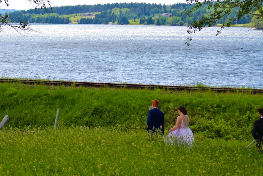 John Ratchford, left, leads the grads down a grassy field next to the Bras d’Or Lakes to the second location for their prom experience photoshoot. NICOLE SULLIVAN/CAPE BRETON POST 