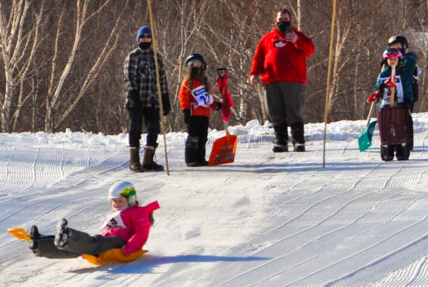 There’s more to Cape Smokey than just skiing and snowboarding as evidenced by a recent downhill shovel race. Above, a young participant slides down the hill on a bright, orange shovel. CONTRIBUTED