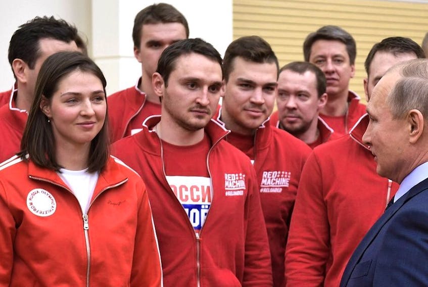 In this image from Russian media taken from Twitter, Vladimir Putin speaks with hockey players from Russia, dressed in Red Machine colours.