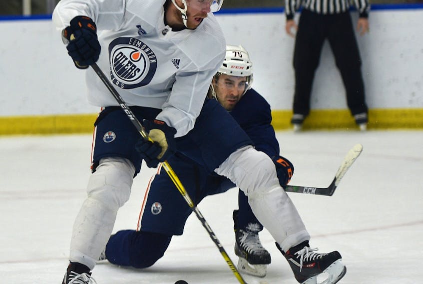 Oilers Connor McDavid (97) tries to shoot the puck with his stick between his legs against Evan Bouchard (75) during training camp at the downtown community rink on Friday, Jan. 8, 2021.