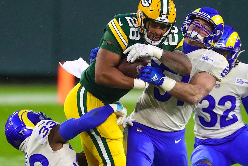 Green Bay Packers running back AJ Dillon (28) runs with the ball while Los Angeles Rams safety Nick Scott (33) and linebacker Troy Reeder (51) attempt to tackle him Saturday at Lambeau Field. 