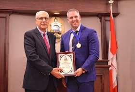 Dr. Wassim Salamoun, left, holds the plaque honouring his co-worker Paul Young at Summerside city hall on Oct. 13. Salamoun read the citation awarding Young the mayor's Medal of Honour. 