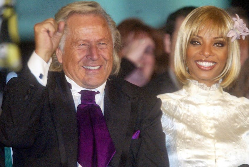 Fashion mogul Peter Nygard, clad in a rich eggplant tie and slick black suit, raises a fist in triumph while sitting front-and-centre at his show with Yves-Lauren.