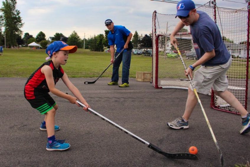 Dylan Thomas, 6, goes head to head with his father Cory, as John Chaisson guards the net during a game of ball hockey at the recent block party arranged by the city to promote community spirit and develop bonds with neighbours.