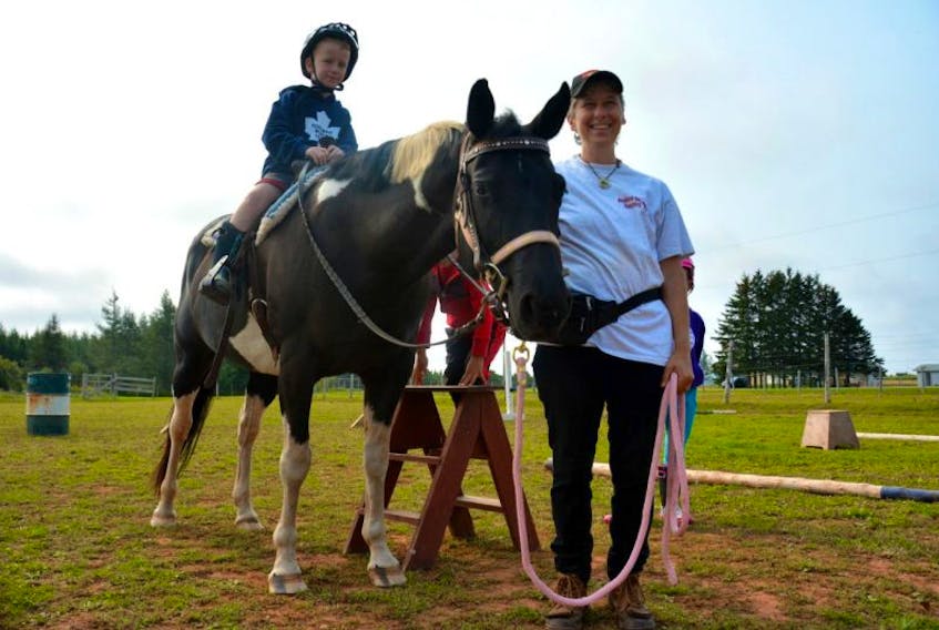Caden MacGregor, from Summerside, climbs on the saddle while Celina Gallant steadies the horse with the reins.