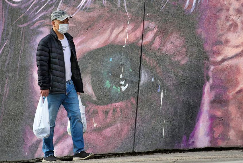 A man wearing a mask carries shopping bags past a mural in downtown Calgary on Monday, April 20, 2020.