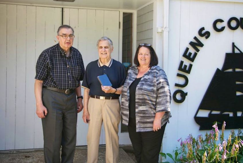 Granville Nickerson poses with his book signed by Babe Ruth, along with George Mitchell, president of the Queens County Heritage Society and Linda Rafuse, manager of the Queens County Museum.