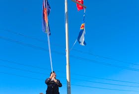 Harry Taylor, second vice-president of Royal Canadian Legion branch 19 in North Sydney, stands on a ladder as he raises the special Remembrance Day flag outside the North Sydney Historical Society on Commercial Street in North Sydney on Tuesday. Assisting Taylor is Joe Meaney, president of the historical society. Chris Connors • Cape Breton