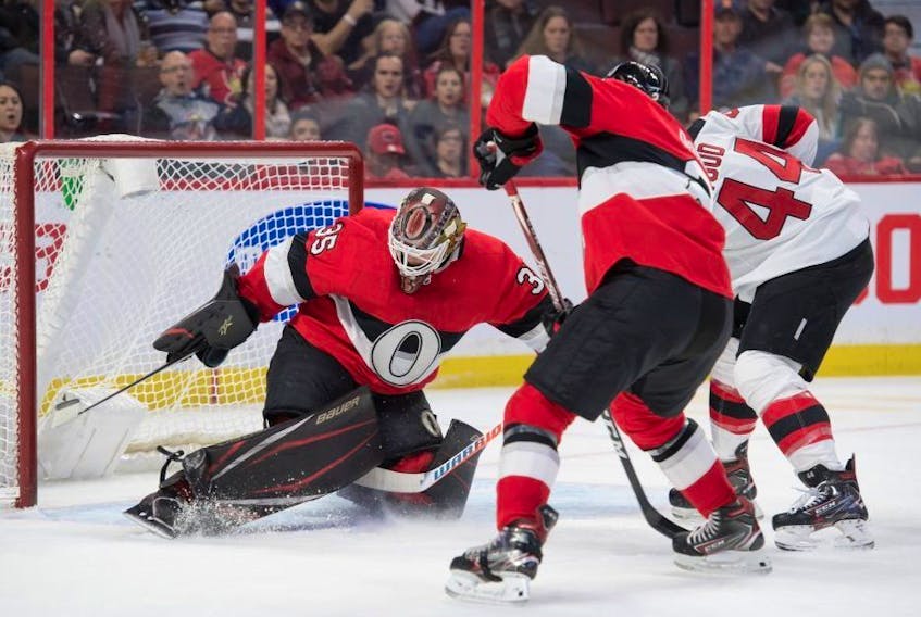Ottawa Senators goalie Marcus Hogberg makes a save in front of New Jersey Devils forward Miles Woods.