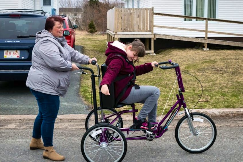 Erica Alcock enjoys riding her new tricycle around the neighbourhood. Her mother Denise controls the bike from a handle in the back.