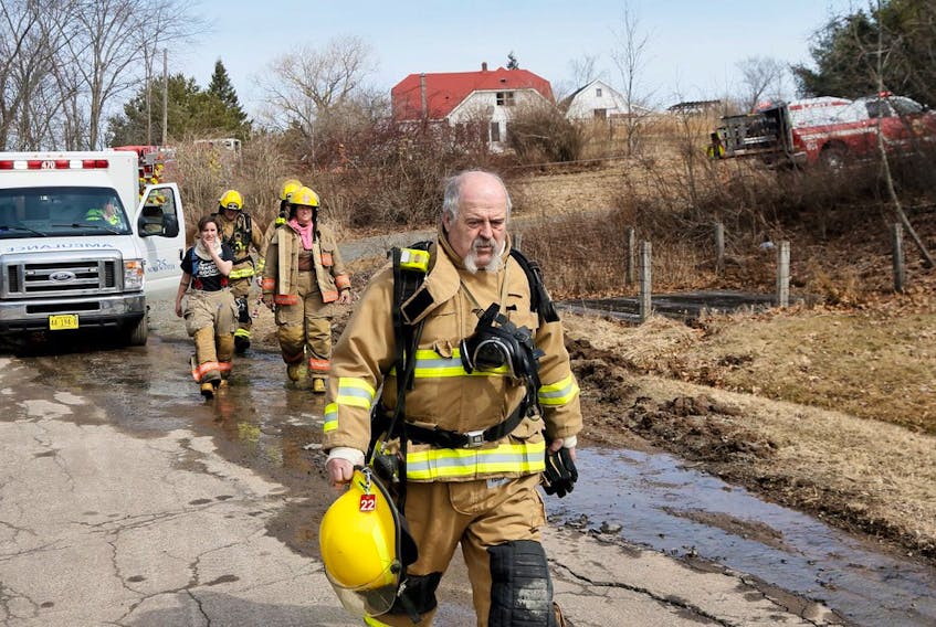 Firefighters walk away from the scene of a fatal house fire in Shubenacadie on Monday afternoon. The home can be seen in the background. – Tim Krochak