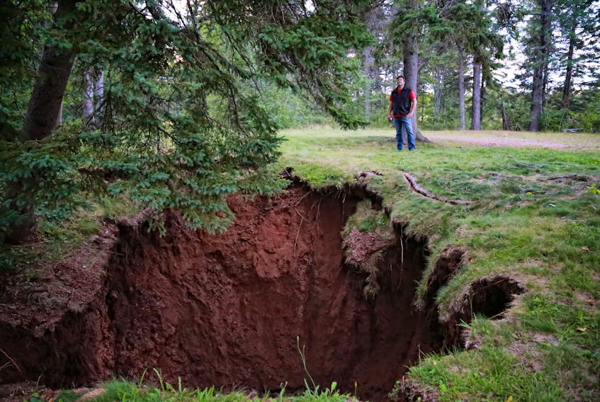 Mark Rushton stands near a large sinkhole that developed in the Oxford Lions Park late Monday evening. There had been a small sink hole there, but it got dramatically bigger last night and it estimated to be 40 to 50 feet wide and 30 or more feet deep with rushing water at the bottom. - Shaun Whalen photo