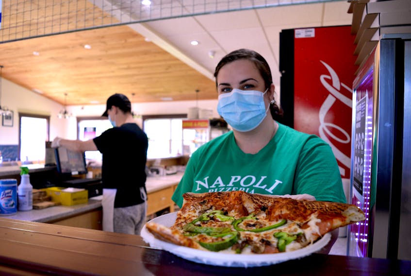 Kate Campbell serves up a hot and fresh slice of pizza on Wednesday at the Napoli Pizza location in Howie Centre. The restaurant has reopened and is now serving customers one at a time through a new takeout window. Gloves and masks are a common site, as well. Going forward the pizzeria will be open Tuesday through Saturday. The Charlotte Street Napoli Pizzeria location remained open during COVID-19 protocols but with additional precautions in place. GREG MCNEIL/CAPE BRETON POST