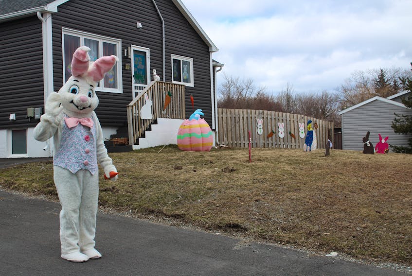 AnnaLee Hyde smiles under the Easter Bunny head as she waves from the front yard of her Glace Bay home on April 11. The teacher assistant and her husband, Dave, decided they wanted to add to their annual holiday decorations as a way to lift people's spirits during the COVID-19 pandemic. Dave made a number of Eastern themed wooden cutouts  (seen in the back of this photo) and AnnaLee called around to find an Easter Bunny suit and checked with authorities first to see if she'd be abiding by the orders in the Health Measures Act put in place to stop the coronavirus that causes COVID-19. After getting the okay and the suit, AnnaLee posted on her Facebook she would be on the lawn from 1 p.m. - 4 p.m. for those driving by. Cars honked as many people waved, some slowing down so the children with the wide smiles in the backseats could wave excited and get a better look at the Easter Bunny. "It gets people's minds off of this COVID thing," Dave said. "It perks everybody up." NICOLE SULLIVAN/CAPE BRETON POST 