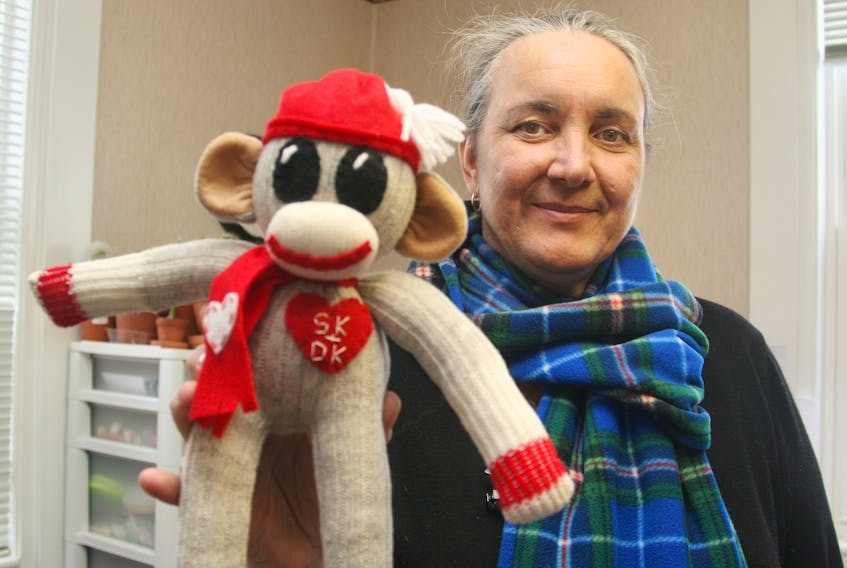 Sock monkey creator and owner of monkeysandmore.com, Sherrie Kearney, holds up one of her latest creations, a Valentine's Day monkey, while wearing another new creation, an eight-foot, tartan, fleece scarf.