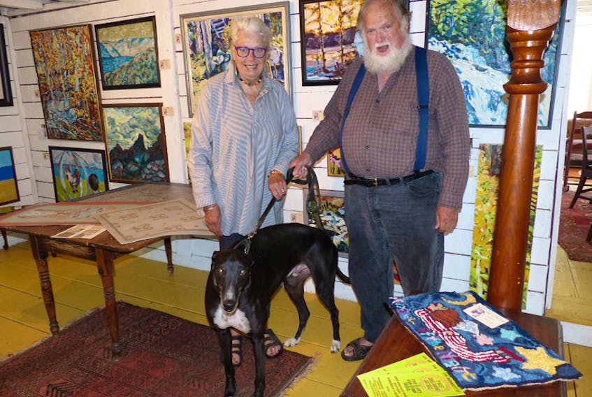Diana Butler and Dennis Teakle stand with their dog, Thor, inside the Shelburne Artery, the art gallery they opened on June 22. Teakle’s paintings are hung in the background, with one of Butler’s hooked rugs displayed in the lower right corner.