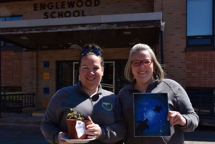 Tara MacKean, left, and her sister, Cheryl Newcombe. hold a tomato plant and a finished painting outside Englewood School, one of the two schools they use for the school age program they run at Merry Pop-Ins Childcare Centre in Tryon. 