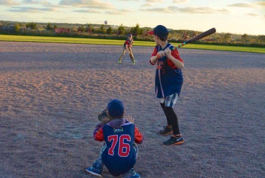 <p>Mitchell Burns throws a pitch across the plate to his older brother, Kendall, as their younger sister, Shelby, plays catcher. The three children played their first season of baseball this past summer in Bedeque.</p>