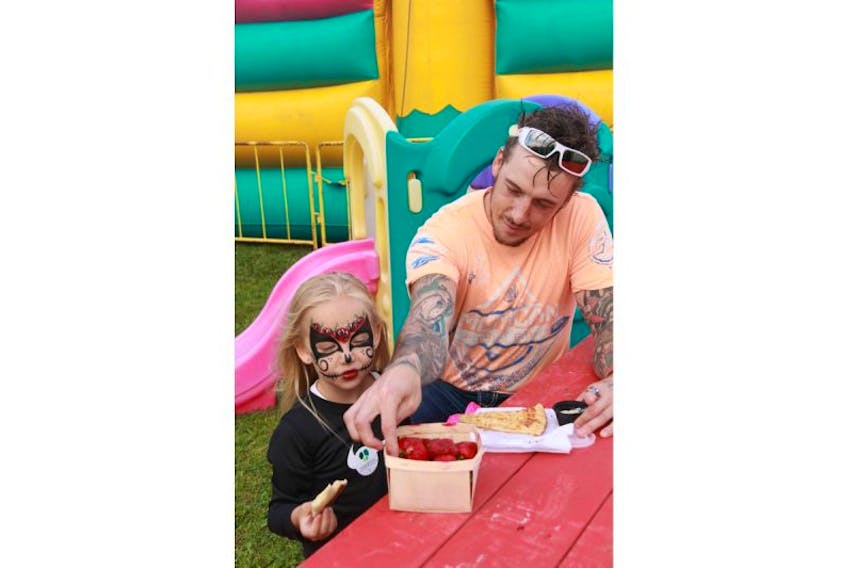 Faith Rumbolt-King and her dad Chad King enjoy strawberries in the Treehouse Family Resource Centre area at the 33ed annual Deer Lake Strawberry Festival on Friday.