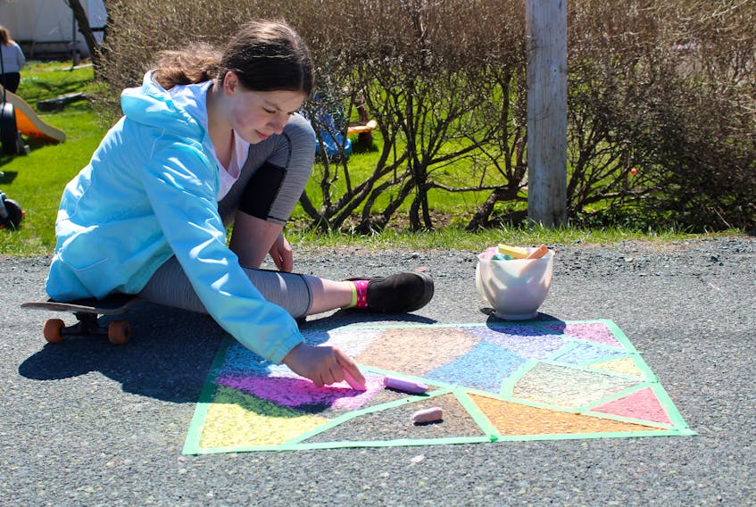 Lily MacIntyre sits on her skateboard while using chalk to create some colourful art on the street in front of her home in Westmount on Sunday. The 13-year-old said she was doing it for fun and to cheer up anyone who sees it when they walk by. Chris Connors/Cape Breton Post