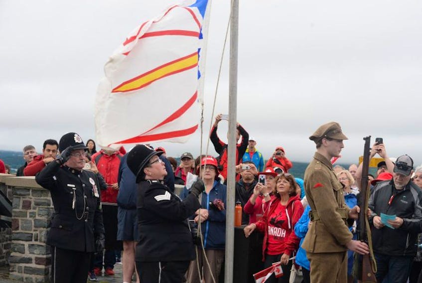 <p>RNC Sgt. Bob Howard salutes to the singing of the “Ode To Newfoundland” as RNC Sgt. Sandy Harvey raises the Newfoundland flag. Shown at right is Hawkin Webber-Windsor, dressed in periodic uniforms that would have been worn by members of the Royal Newfoundland Regiment, circa 1916.</p>
