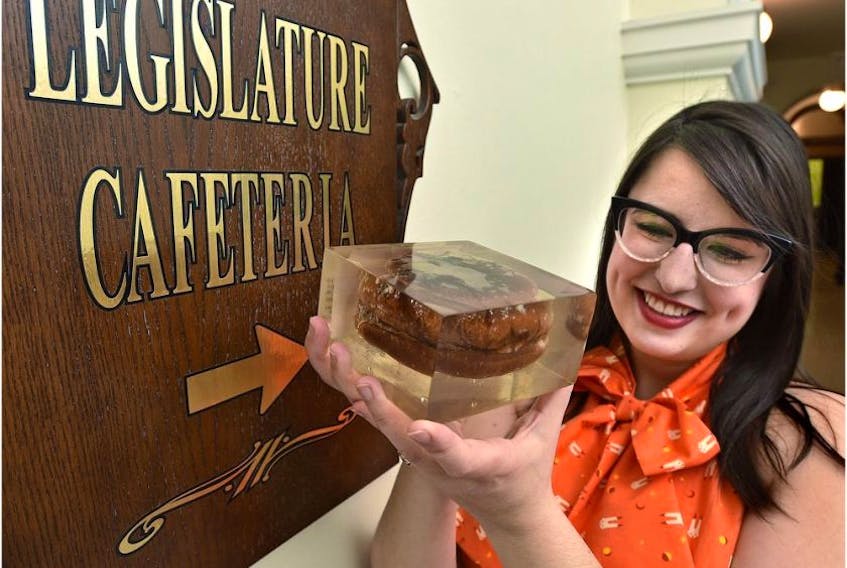 Kelsey Kendrick, program assistant Visitor Services, holding the famous resin-encased hamburger that is housed in the Alberta Legislature library, and their celebrating its 50th birthday by throwing it a party, having a large burger-shaped cake and food-themed tours all at the Federal Building in Edmonton, March 21, 2019. - Ed Kaiser