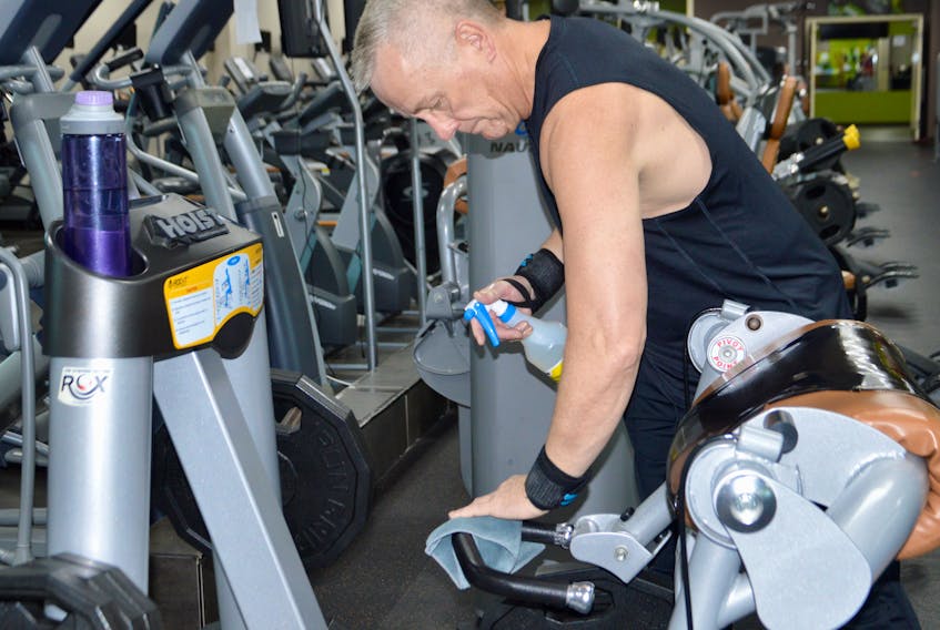 Father Paul Murphy carefully sanitizes the fitness equipment he has just used so the next person will be able to use a clean machine, just part of the requirements for those exercising at Ascendo Fitness/Supplement King in Sydney. ELIZABETH PATTERSON/CAPE BRETON POST