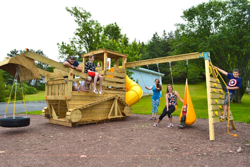 Albert MacKay, from left, relaxes on a bulldozer playset with his wife Elaine, son Brian, neighbour Noline Francis and her children Kaley, 21, Jolton, 3, and Jaron, 12. MacKay built the playset for Francis to pay her back for showing up with dinner for him every night while Elaine and Brian were in Halifax for Brian’s cancer treatment. Sharon Montgomery-Dupe/Cape Breton Post