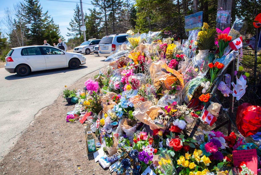 RCMP officers speak with a visitor near the large memorial in memory of the victims from the mass shooting seen at Portapique Beach Road in Portapique, N.S., on Thursday, April 30, 2020.