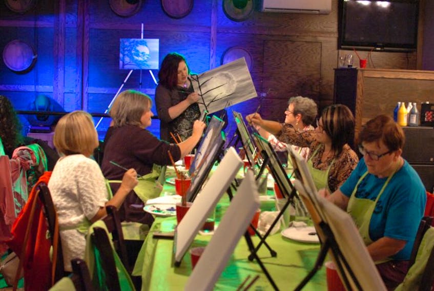 Instructor Emma Dooley guides participants in painting Teal Tree in the Moonlight during a recent Paint Nite class at Shenanigan’s bar in Foxtrap.