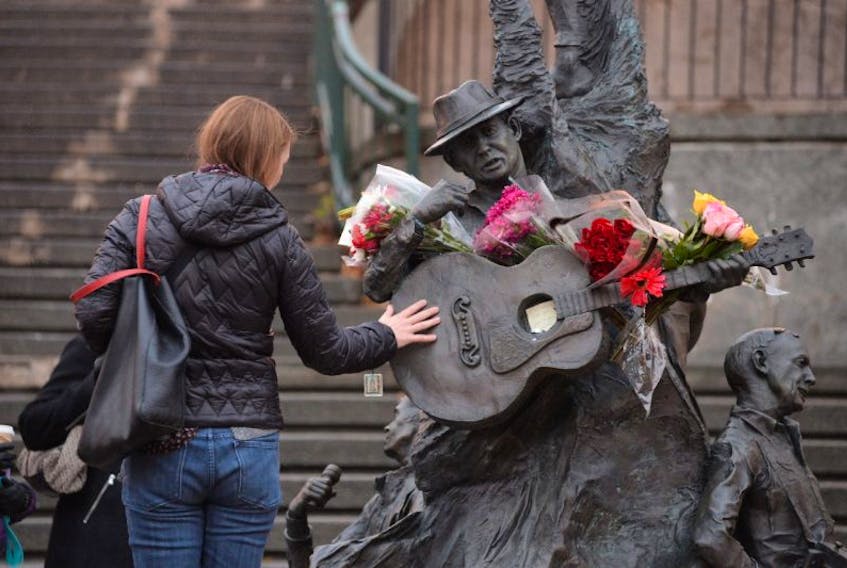 A woman places her hand on the guitar on the statue of Ron Hynes on George Street.