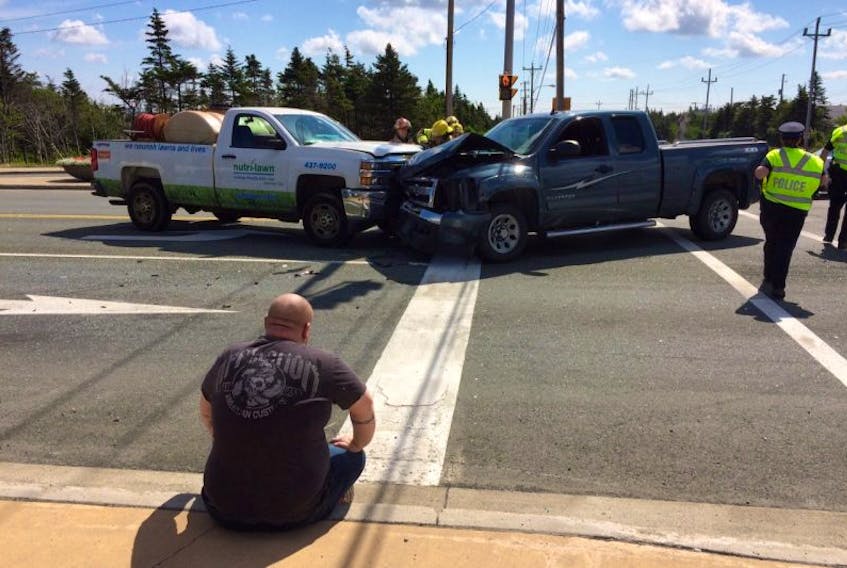The driver of a pickup truck sits on the curb after his vehicle collided with two others at the intersection of Richard Nolan Drive and Old Placentia Road in Mount Pearl Friday morning. Firefighters are seen prying open the hoods of the trucks to cut wires to the batteries.
