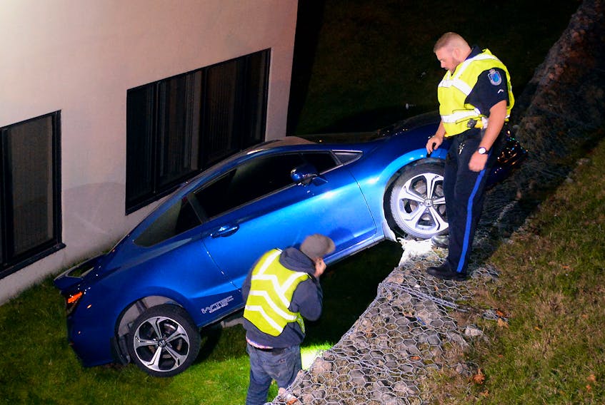 A tow truck operator from Avalon Towing and an officer with the Royal Newfoundland Constabulary examine a car that went driverless over an embankment Sunday night.