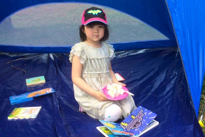 Weixi Dong , 5, enjoys a treat of cake as she looks at books in the reading tent. on the lawn of the Arts and culture centre Saturday just past noon. Weixi was attending the TD Summer Reading Event at the A.C. Hunter Children's Library with her mother, Shuang Dong.