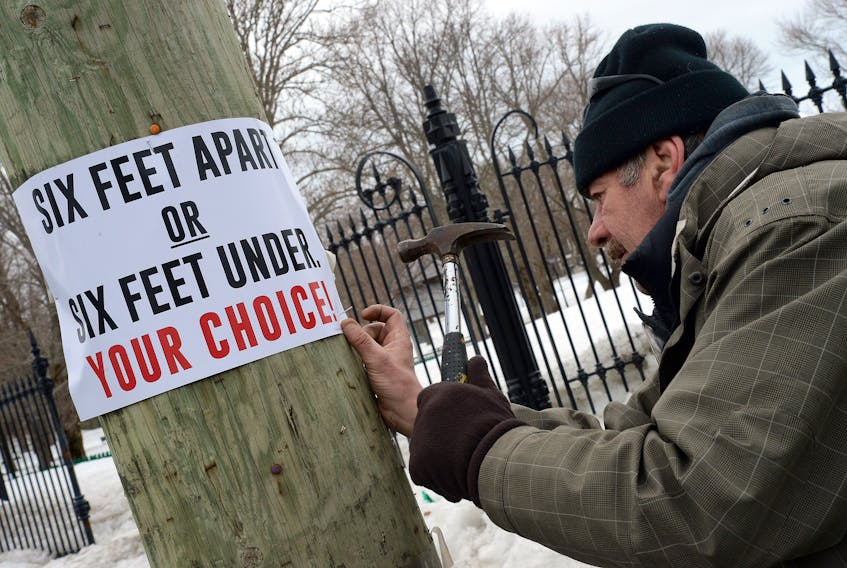 Paul Hartery nails a sign to a utility pole in the downtown area of St. John’s Monday afternoon. The signs remind people of physical distancing guidelines, and possible consequences of not following them, during the Covid-19 crisis.

Keith Gosse/The Telegram