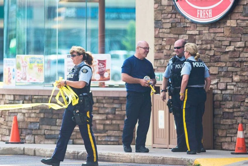 A RCMP officer removes the yellow police tape as Cpl. Ron Robinson, centre, RCMP explosives expert, Const. Lorenz Sanders and Sgt. Leanne Butler, examine the smoke detector that caused the evacuation of the Stratford Petro-Canada/Tim Hortons Sunday. The smoke detector was in a plastic bag and making 'suspicious" sounds so as a precaution the Explosive Disposal Unit was called in from Halifax.