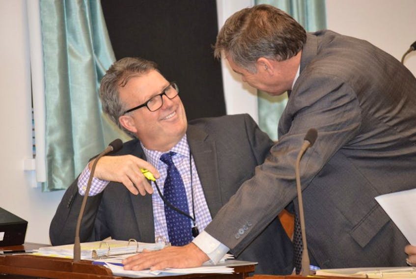 Doug Currie, left, minister of education, early learning and culture and Robert Mitchell, minister of communities, land and environment, discuss business before the Wednesday session of the P.E.I. legislature.