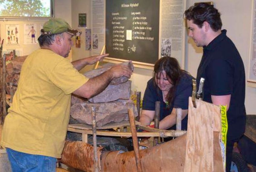 Mi’kmaw canoe builder Todd Labrador, left, and apprentices Melissa Labrador and Kyle Gloade use rocks to shape the gunwales of the birch bark canoe tthat was built at the Millbrook Cultural and Heritage Centre in Nova Scotia.