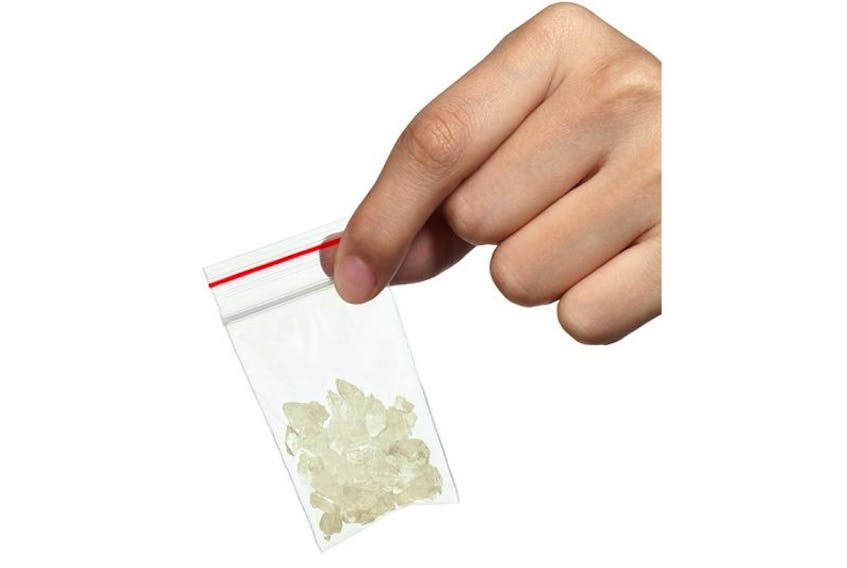 A hand holding a bag with white crystals in it, similiar to methamphetmines, or crystal meth.