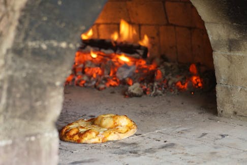 A traditional pizza is shown cooking on the wood fire of the Margaree Community Oven. After its first official season last year, a volunteer committee is looking forward to many more meals shared around the hearth by residents and families.