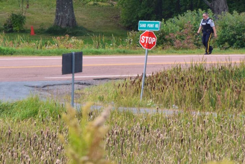 A police officer walks on the road near the scene of a gunfire exchange at Lockerbie Memorial Cemetery between RCMP and a Bayhead man.