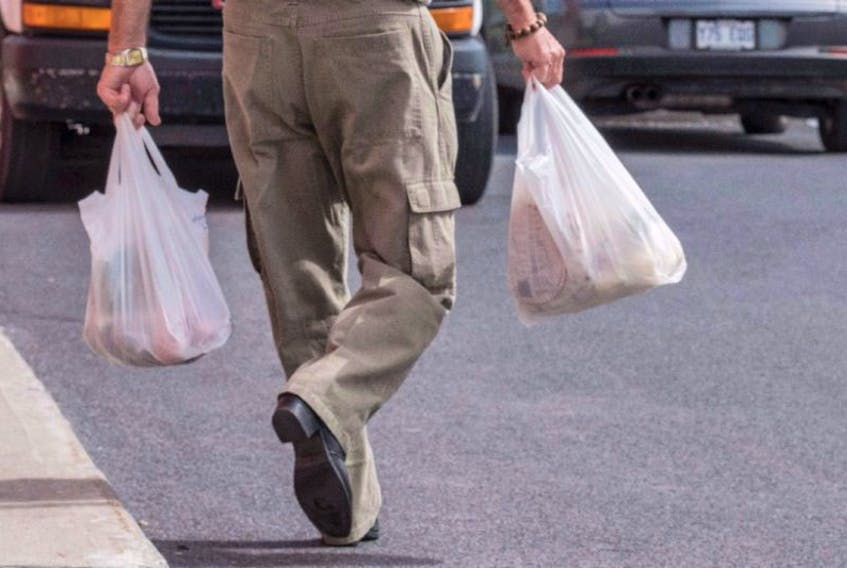 A shopper leaves a grocery store carrying his groceries in plastic bags.