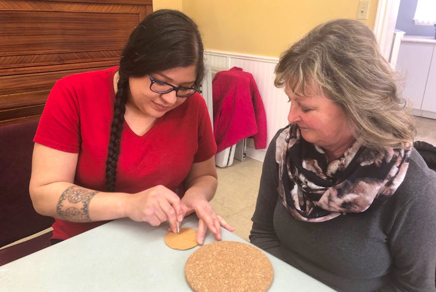 Kathy Peters, right, of St. Charles, PEI, watches as quillwork instructor Melissa Peter-Paul pokes holes in a piece of birch bark in preparation for making an eight-pointed star design.  
