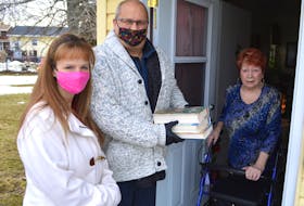 Jim Kronlund of North Sydney and volunteer Lisa Pelland, left, drop off books to Carole Smith of Glace Bay, who has mobility issues and difficulty getting out, as part of the new Capers Community Books Facebook volunteer group Kronlund started. Kronlund said anyone can stop by his house on Stanley Street in North Sydney to sign out a book. Sharon Montgomery-Dupe/Cape Breton Post